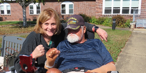 a woman and a man in a wheelchair embrace in front of a building